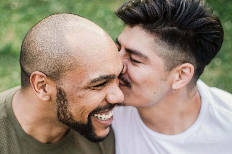 a couple of men standing next to each other, by Arabella Rankin, trending on pexels, kissing smile, shaved beard, mixed race, multicoloured