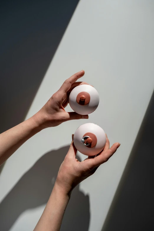 a person holding two white balls in their hands, an abstract sculpture, trending on unsplash, photorealism, mirror eye implants, animal eyes, trending on dezeen, made of glazed