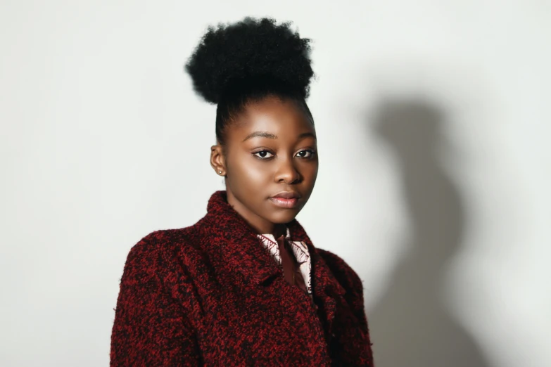 a woman standing in front of a white wall, trending on pexels, renaissance, black teenage girl, topknot, red coat, studio portrait