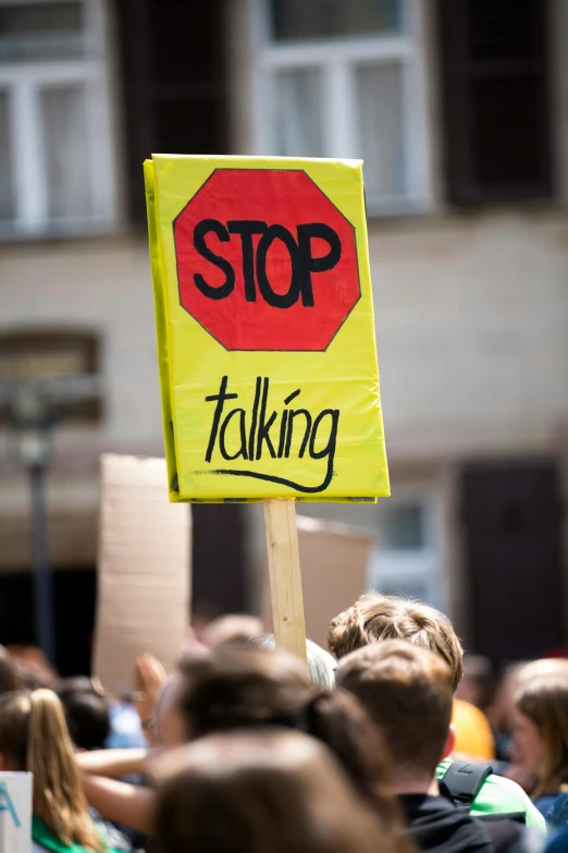 a group of people holding signs in front of a building, by Jan Tengnagel, shutterstock, negative self-talk, vitalik buterin, wearing a stop sign on its head, brown