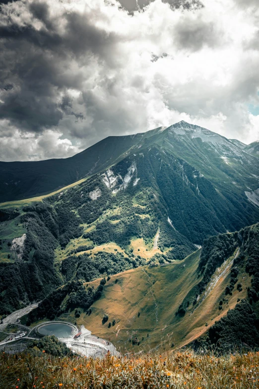 a man standing on top of a lush green hillside, by Sebastian Spreng, unsplash contest winner, baroque, “ aerial view of a mountain, dark clouds above, destroyed mountains, tall mountain