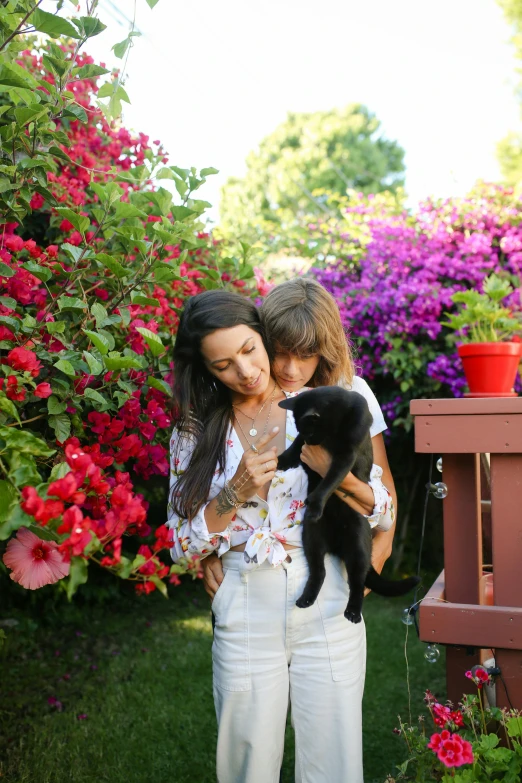 a woman holding a small black dog in her arms, by Julia Pishtar, garden with flowers, aurora aksnes and zoë kravitz, petting a cat, family photo