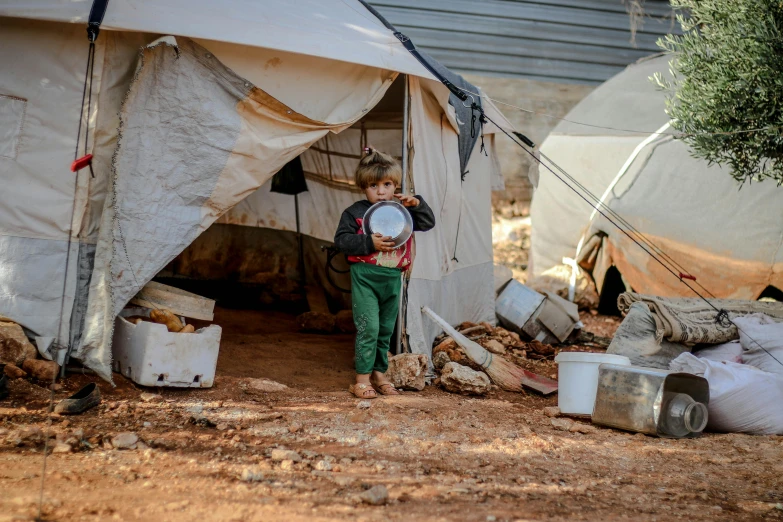 a little boy standing in front of a tent, by Meredith Dillman, hurufiyya, people outside eating meals, rust and plaster materials, photograph taken in 2 0 2 0, holding a shield