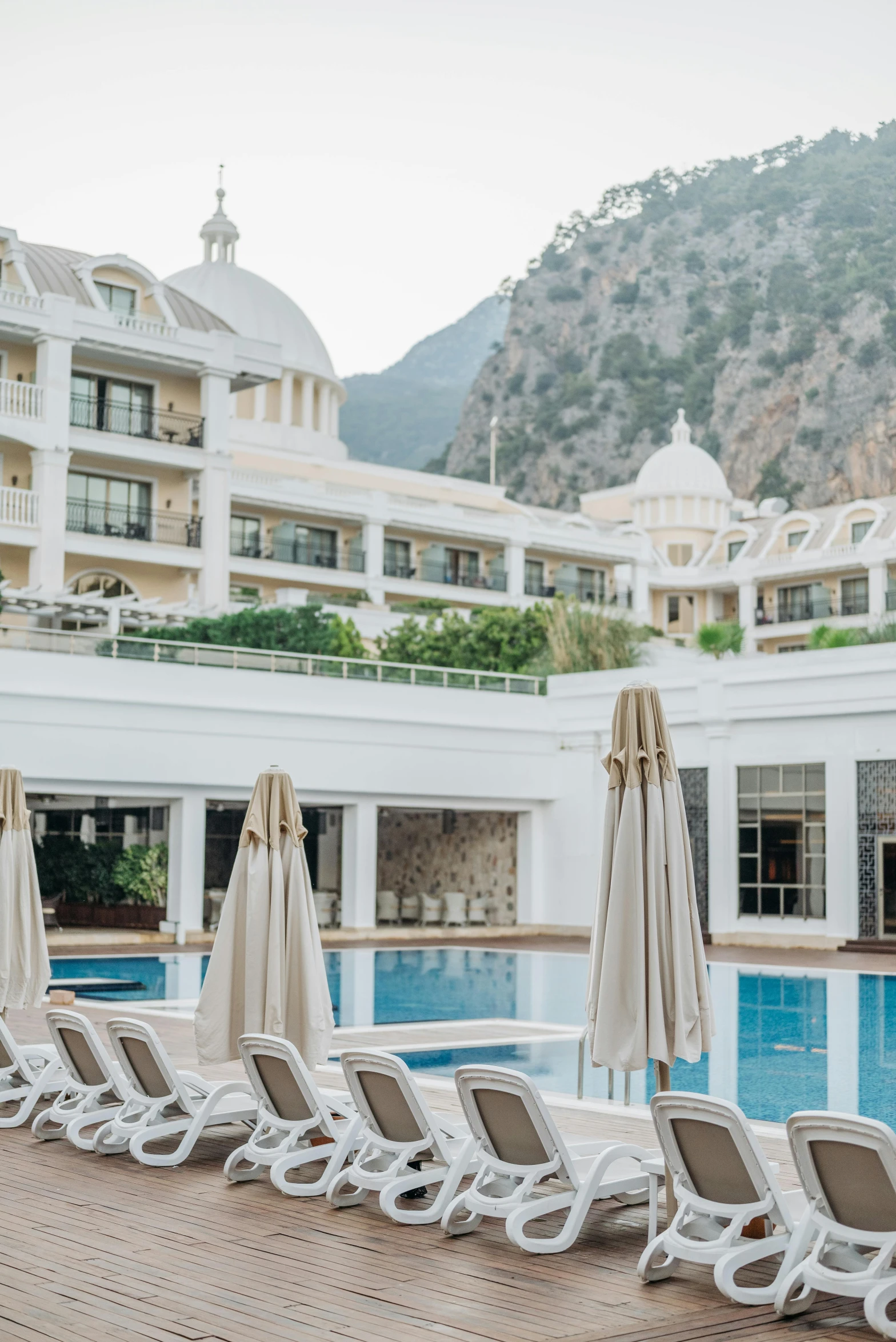 a row of lounge chairs sitting next to a swimming pool, art nouveau, grand majestic mountains, turkey, multiple stories, white robe with gold accents