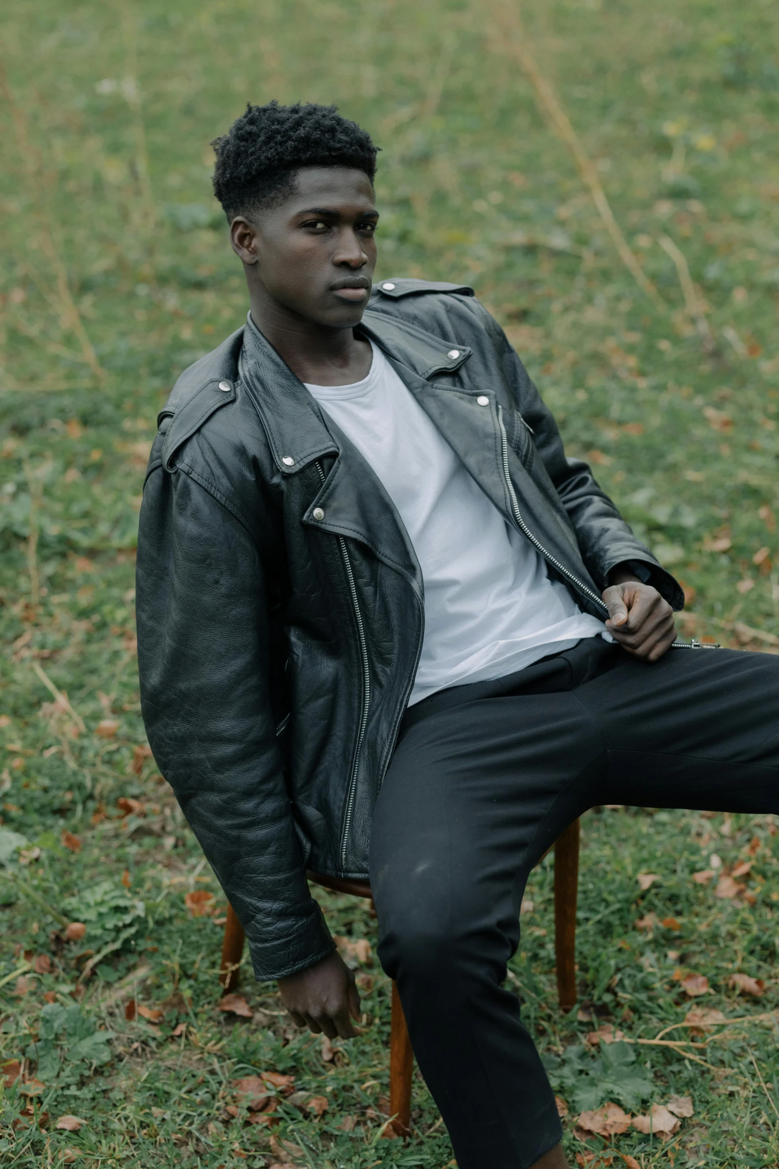 a man sitting on top of a wooden chair, inspired by Theo Constanté, trending on pexels, realism, black leather jacket, ( ( dark skin ) ), male teenager, virgil abloh