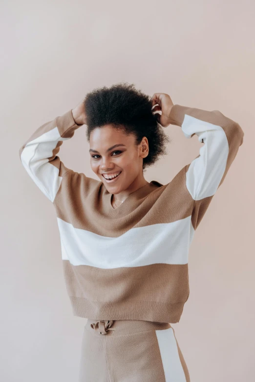 a woman standing with her hands on her head, inspired by Esaias Boursse, trending on pexels, minimalism, brown sweater, happy fashion model, striped, natural hair