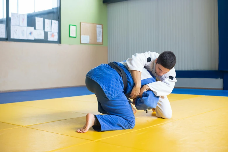 a man that is kneeling down on a mat, white belt, engaging, blue, sports setting