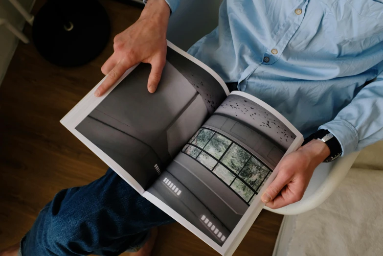 a man sitting in a chair holding a book, pexels contest winner, photorealism, architectural magazine, printed page, lit from above, soft vinyl