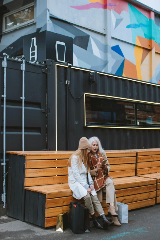 a woman sitting on a bench in front of a building, trending on unsplash, graffiti, shipping containers, behind bar deck with bear mugs, toddler, kombi