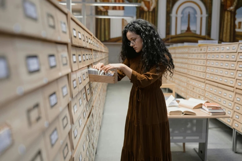 a woman standing in front of a wall of drawers, an album cover, academic art, inspect in inventory image, wearing a brown cape, book library studying, fernanda suarez