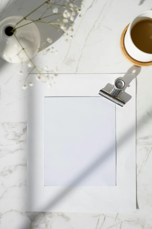 a picture frame sitting on top of a table next to a cup of coffee, inspired by Agnes Martin, trending on pexels, holding a clipboard, clean white paper background, polished white marble, light scatter