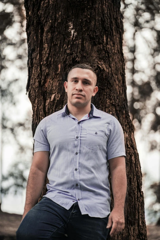 a man sitting on a bench next to a tree, an album cover, inspired by Carlos Berlanga, pexels contest winner, hurufiyya, serious look, young adult male, portrait of forest gog, standing