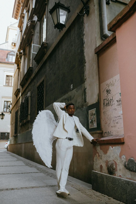 a man in a white suit walking down a street, pexels contest winner, baroque, grand angel wings, leaning on the wall, lgbtq, berlin fashion