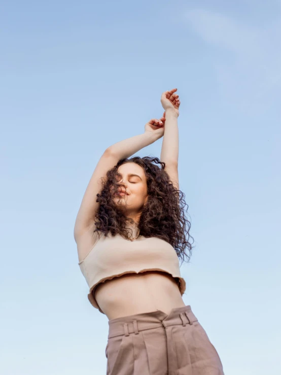 a woman standing on top of a lush green field, an album cover, trending on pexels, renaissance, armpit, clear sky, brown curly hair, modern dance aesthetic