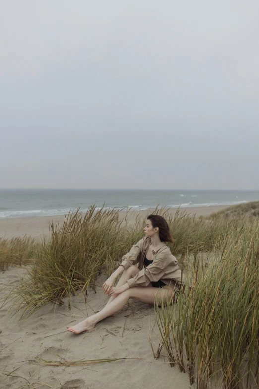 a woman sitting on top of a sandy beach, a picture, unsplash, conceptual art, with soft bushes, belgium, 8 k -