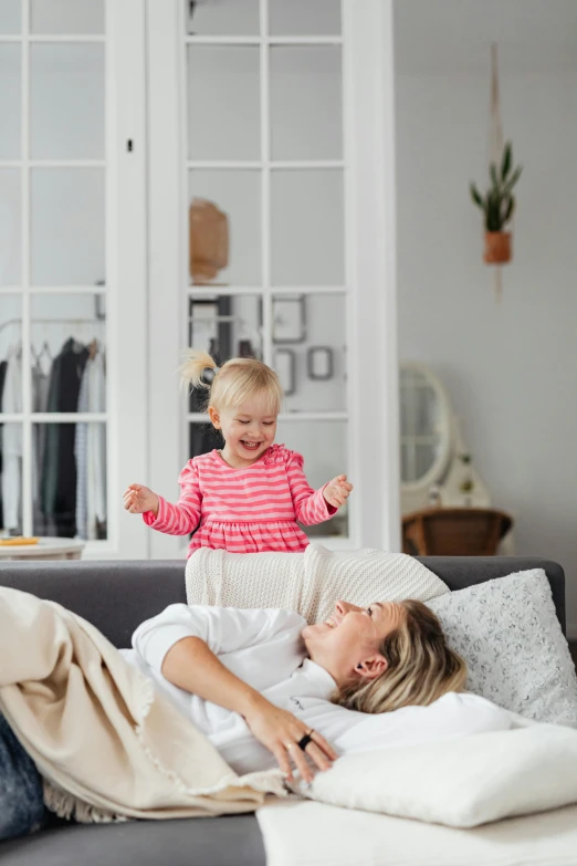 a woman laying on top of a couch next to a child, happy atmosphere, bedhead, with arms up, clean design