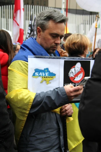a man holding a sign in front of a crowd of people, inspired by Dariusz Zawadzki, snapchat, ukrainian flag on the left side, holding a smoking ray-gun, praying