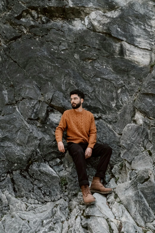 a man sitting on top of a large rock, a portrait, by Adam Dario Keel, pexels contest winner, renaissance, brown sweater, natural beard, black and terracotta, full body photo of steve