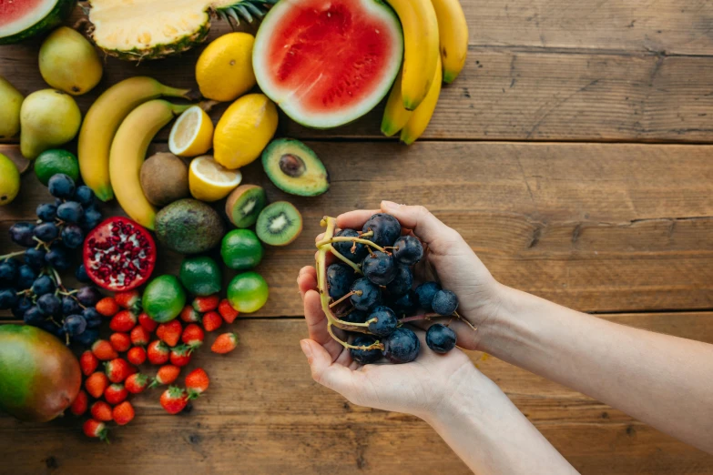 a person holding a bunch of fruit on top of a wooden table, background image, profile image