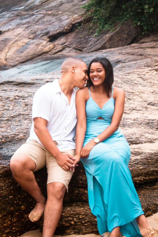 a man and woman sitting on a rock in front of a waterfall, posing on the beach, light blue dress portrait, manly, profile image