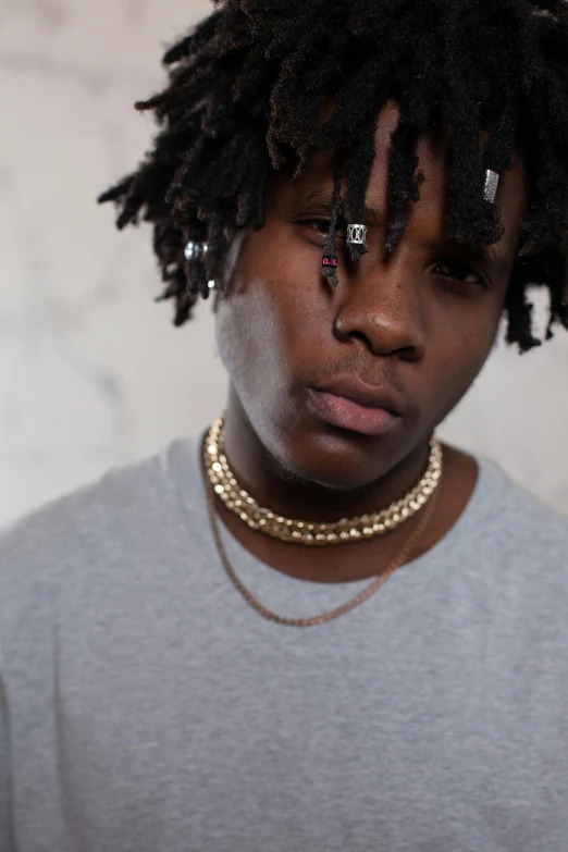 a man with dreadlocks standing in front of a wall, an album cover, trending on pexels, wearing gold detailed choker, chief keef, ( ( theatrical ) ), sad look