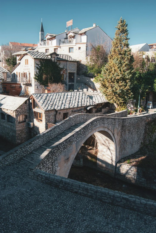 a stone bridge over a river with buildings in the background, bosnian, top - down photo, tiled roofs, 2022 photograph