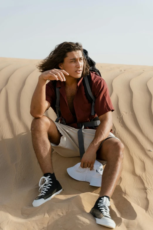 a man sitting on top of a sand dune, trending on pexels, renaissance, dark brown hair and tan skin, a man wearing a backpack, with long curly hair, official store photo