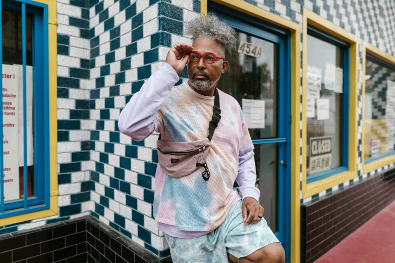 a man that is standing in front of a building, trending on pexels, george clinton, pastel clothing, bra and shorts streetwear, malcolm hart