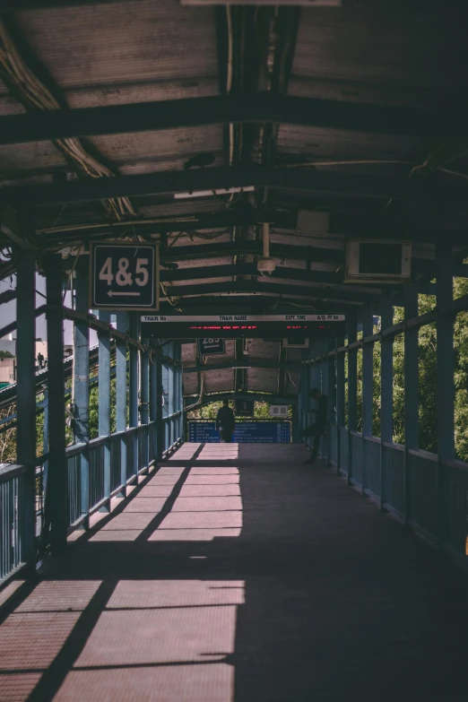 a man sitting on a bench in a train station, unsplash, hell gate, standing on a bridge, sunfaded, overhead canopy