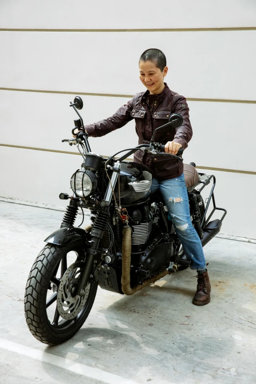 a woman sitting on a motorcycle in front of a garage, wearing brown leather jacket, triumph, in sao paulo, <wearing brown leather armor>