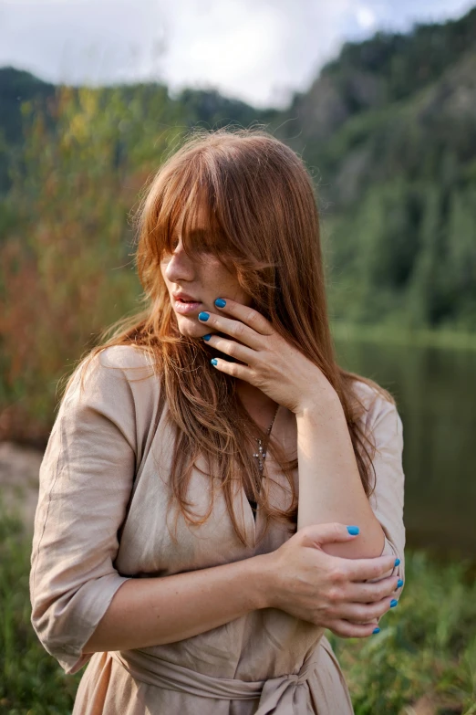 a woman standing next to a body of water, an album cover, inspired by Elsa Bleda, trending on pexels, renaissance, painted nails, beautiful redhead woman, with a brown fringe, in the countryside