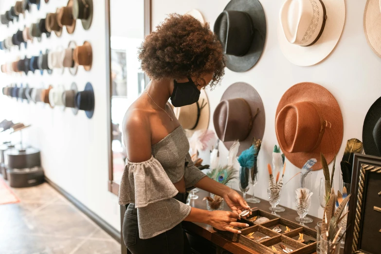 a woman standing in front of a wall of hats, a cartoon, trending on pexels, renaissance, jewelry display, inspect in inventory image, brown, mask