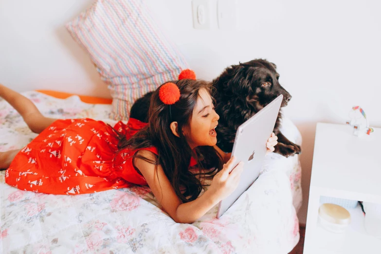 a little girl laying on a bed with a laptop, by Julia Pishtar, pexels, dog, girl wears a red dress, using a magical tablet, couple on bed