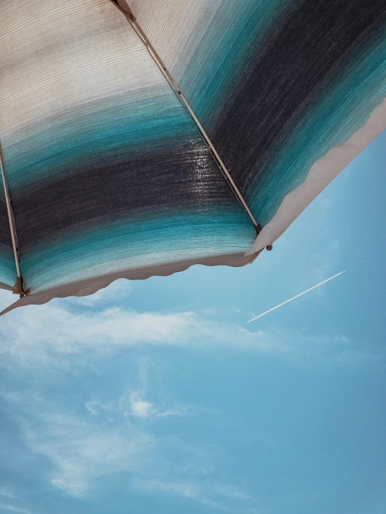 an open umbrella sitting on top of a sandy beach, by Niko Henrichon, unsplash contest winner, light and space, flying through the sky, awnings, profile image, black and teal paper