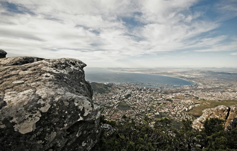 a large rock sitting on top of a lush green hillside, by Daniel Lieske, pexels contest winner, the sea seen behind the city, royal cape, hazy and dreary, fresh from the printer