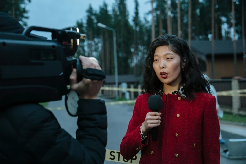 a woman holding a microphone in front of a camera, by Jaakko Mattila, evening news program, gemma chan, emergency, shot on sony a 7