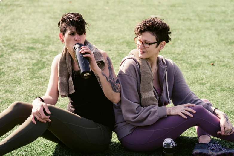 a couple of women sitting on top of a lush green field, a portrait, by Nina Hamnett, pexels, drink milkshakes together, wearing fitness gear, avatar image, non-binary