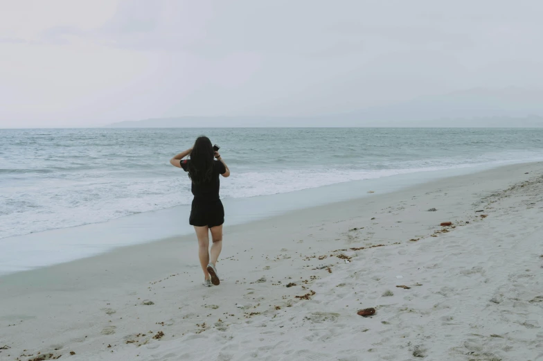 a woman walking on a beach next to the ocean, a picture, unsplash contest winner, realism, wearing black shorts, background image, vintage photo, full body image