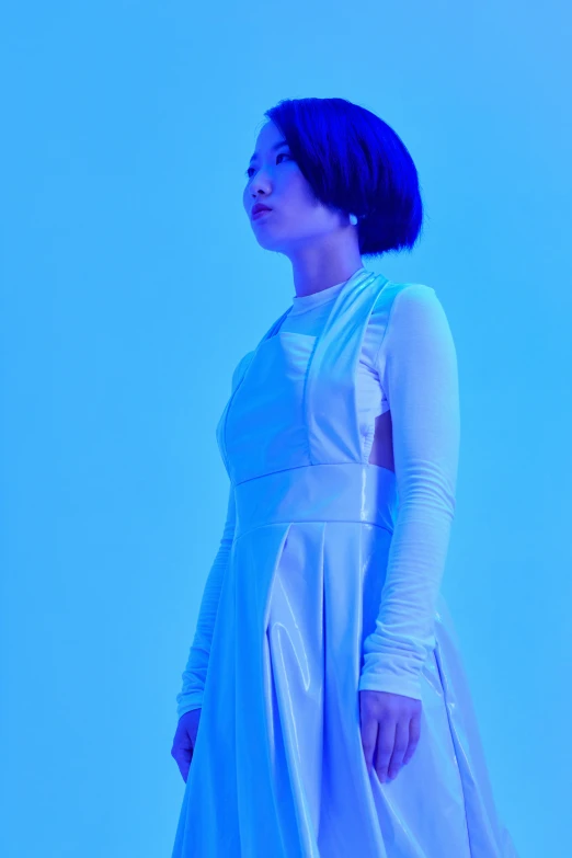 a woman in a white dress standing in front of a blue background, an album cover, inspired by Gao Cen, unsplash, with short hair, wearing atsuko kudo latex outfit, standing in a dimly lit room, ((blue))