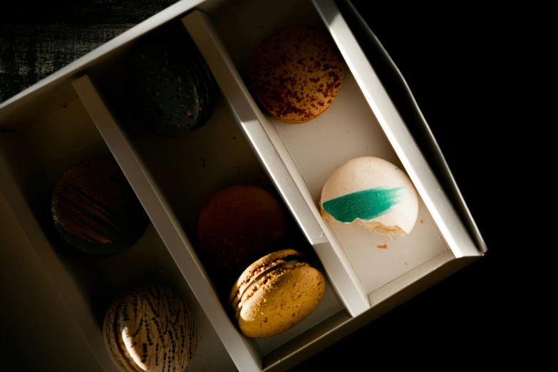 a box of macarons sitting on top of a table, inspired by Charles Le Roux, unsplash, visual art, white and teal metallic accents, dark sienna and white, opening shot, thumbnail