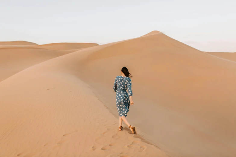 a woman in a blue dress walking in the desert, pexels contest winner, patterned clothing, sand banks, background image, travel guide