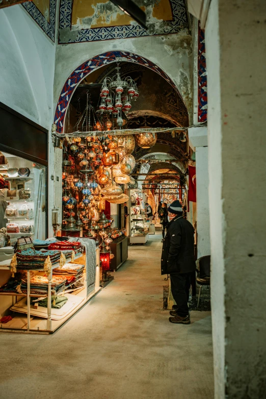 a man standing in front of a store filled with lots of items, trending on pexels, art nouveau, mosque interior, underground city, hanging lanterns, seen from behind