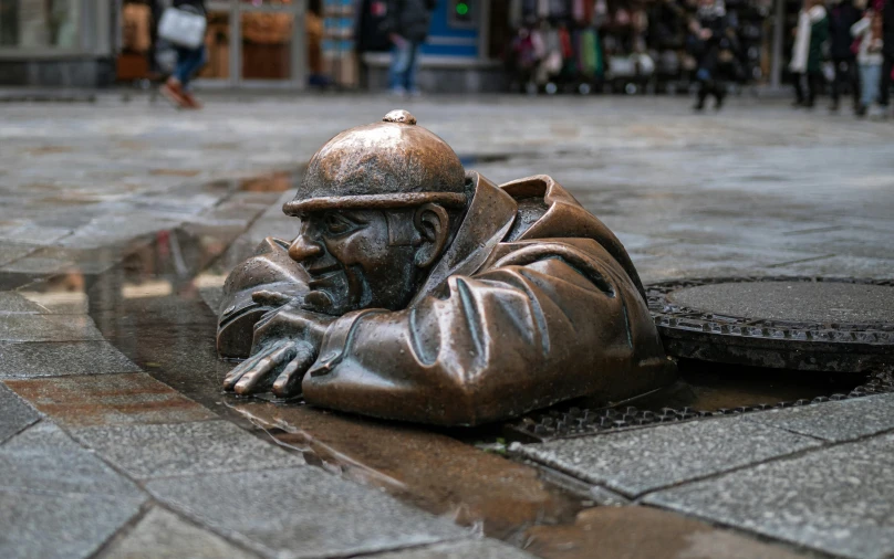 a bronze statue of a man laying on the ground, inspired by Sir Jacob Epstein, pexels contest winner, street art, ireland, aardman studios, walter white hiding in a sewer, where a large