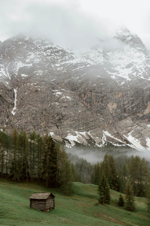 a small cabin in a field with a mountain in the background, inspired by Alberto Sughi, romanticism, lago di sorapis, light grey mist, looking down at the valley, epic ultrawide shot