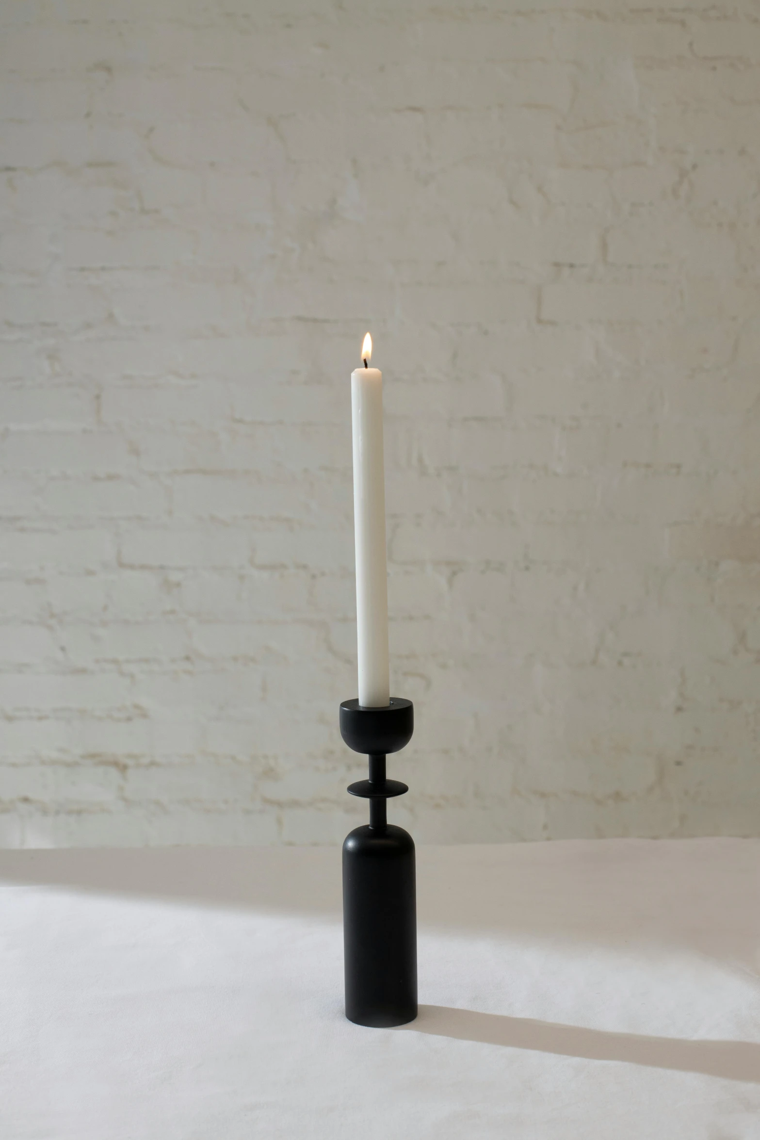 a candle sitting on top of a table next to a brick wall, inspired by Diego Giacometti, folk art, black lacquer, modeled, spire, on a marble pedestal