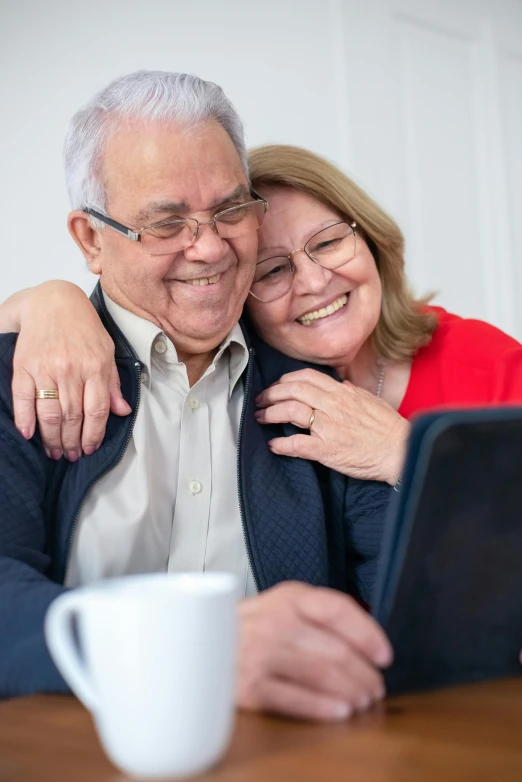 a man and woman sitting at a table with a laptop, taking a selfie, portrait of hide the pain harold, older woman, embracing