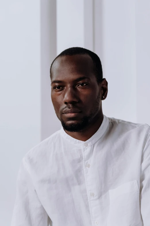 a man in a white shirt sitting down, les nabis, black main color, receding hairline, off - white collection, looking towards camera