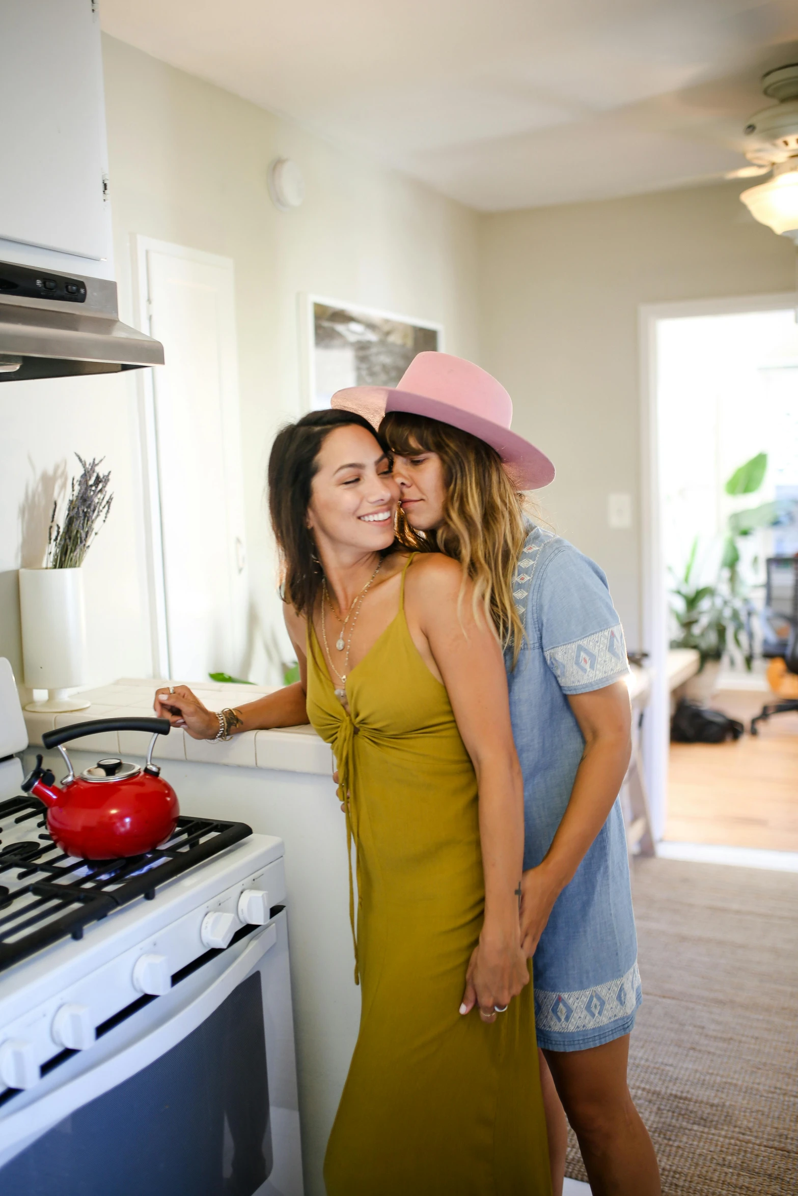 a couple of women standing next to each other in a kitchen, a picture, couple kissing, airbnb, with hat, ariel perez