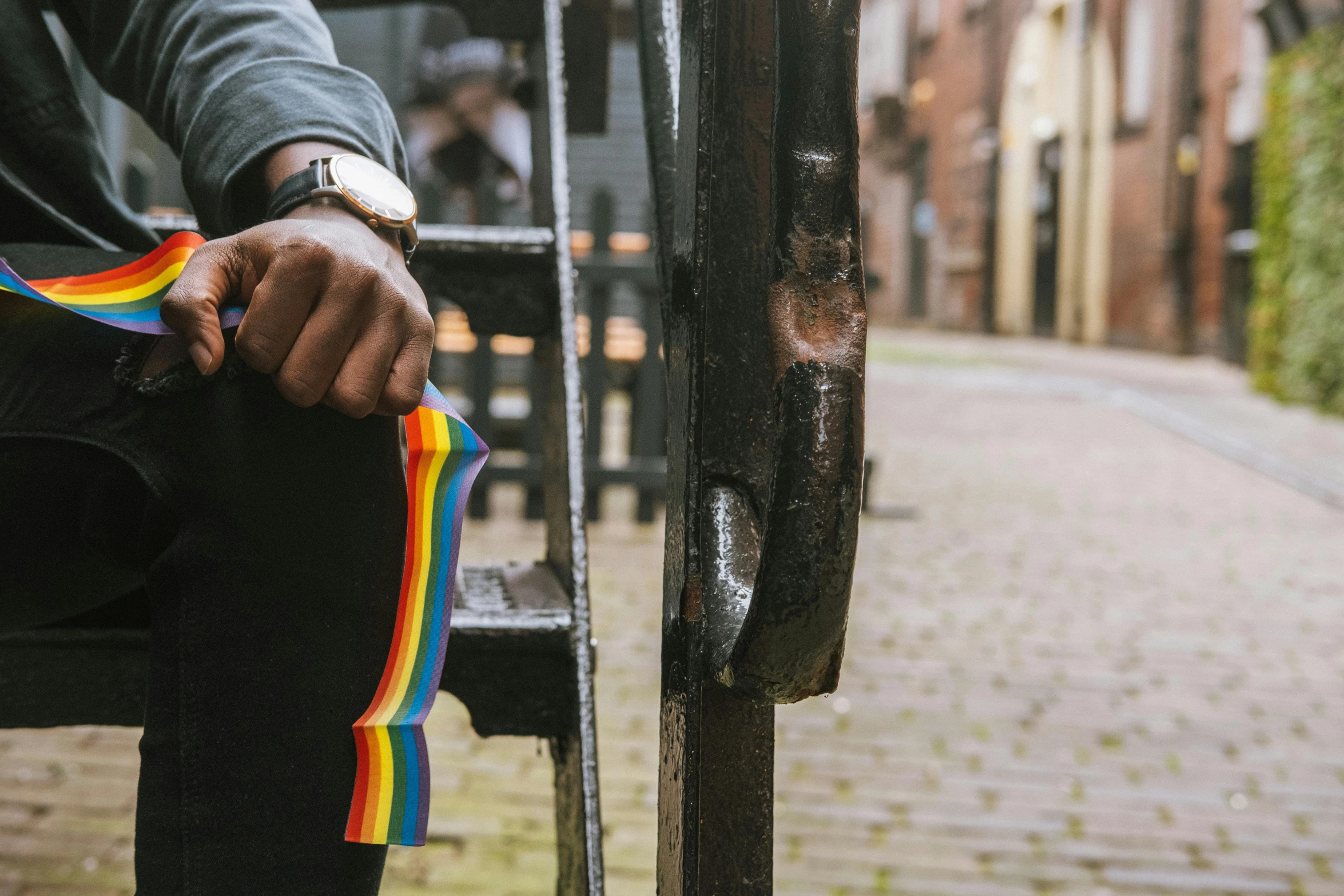 a person sitting on a bench with a rainbow scarf, by Nina Hamnett, unsplash, standing in an alleyway, suspenders, holding trident, about to enter doorframe