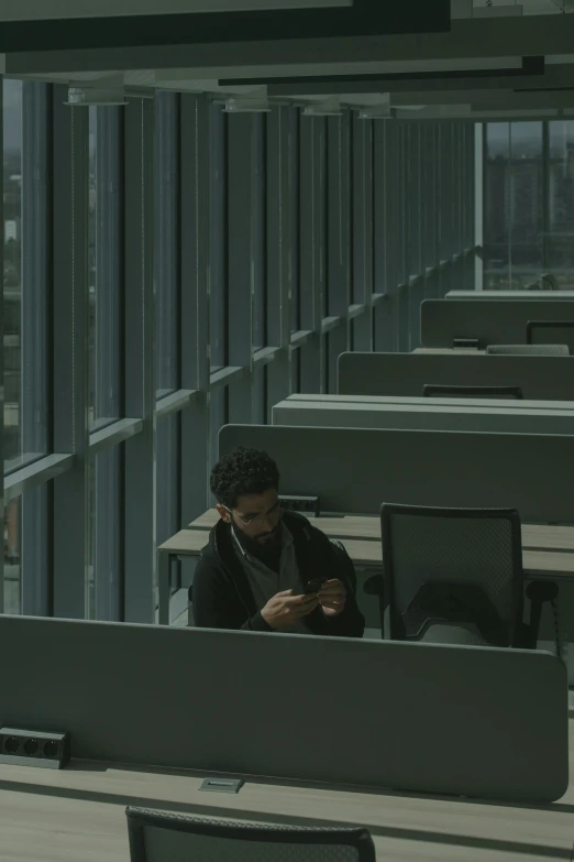 a man sitting at a desk using a cell phone, by Jacob Toorenvliet, pexels contest winner, serial art, endless empty office building, in a movie still cinematic, at college, overcast